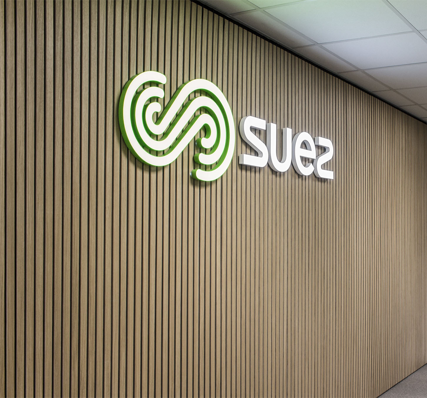 SUEZ - logoskilt på trælistevæg